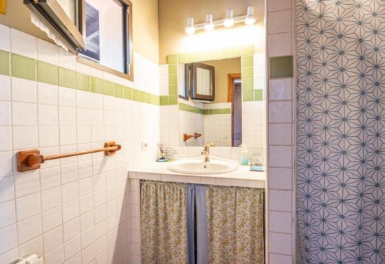 Habitaciones vistas al mar Baño con lavabo, espejo y ducha, decorado en tonos verdes y azules.