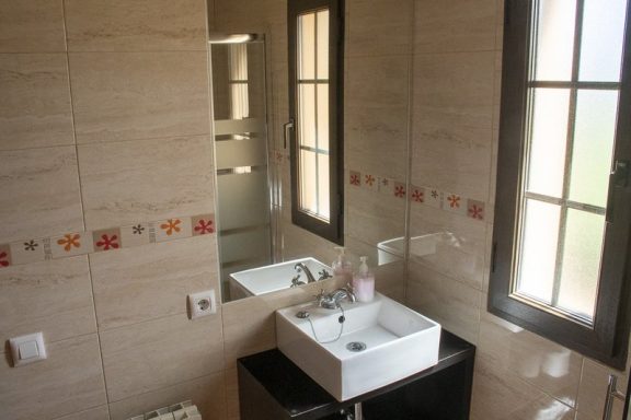 Apartamento Baño moderno con lavabo blanco, espejo y azulejos decorativos. Ventanas iluminan el espacio.