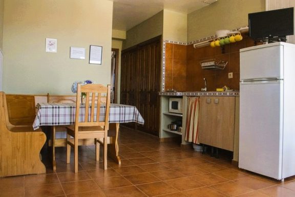 Apartamentos Cocina con mesa, sillas, nevera y utensilios de cocina en un ambiente acogedor.