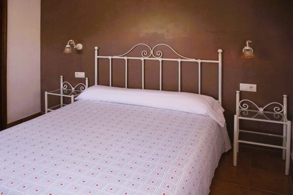 Apartamentos Cama doble con sábanas blancas y cabecero metálico en habitación sencilla.