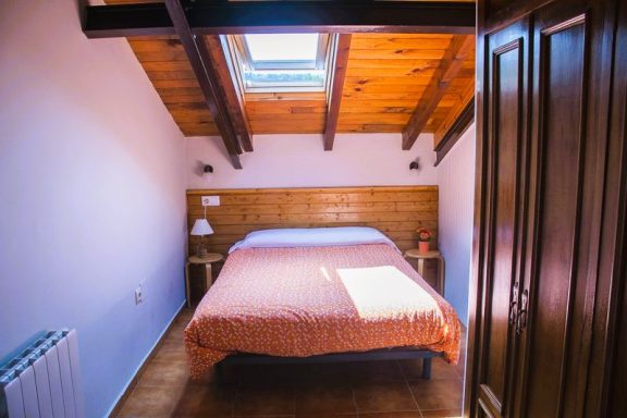 Buhardilla Dormitorio con cama grande, techos de madera y ventana al techo, luz natural.