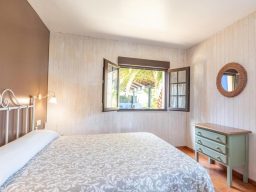 Habitación iluminada con cama, ventanal y cómoda verde. Decoración sencilla y acogedora.