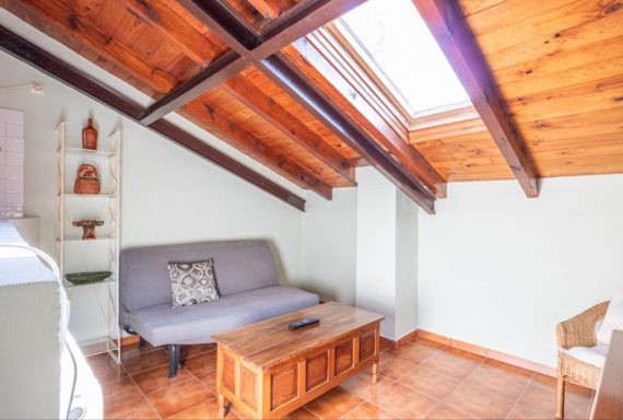 Buhardilla Sala de estar iluminada con sofá gris, mesa de madera y vigas de madera expuestas.